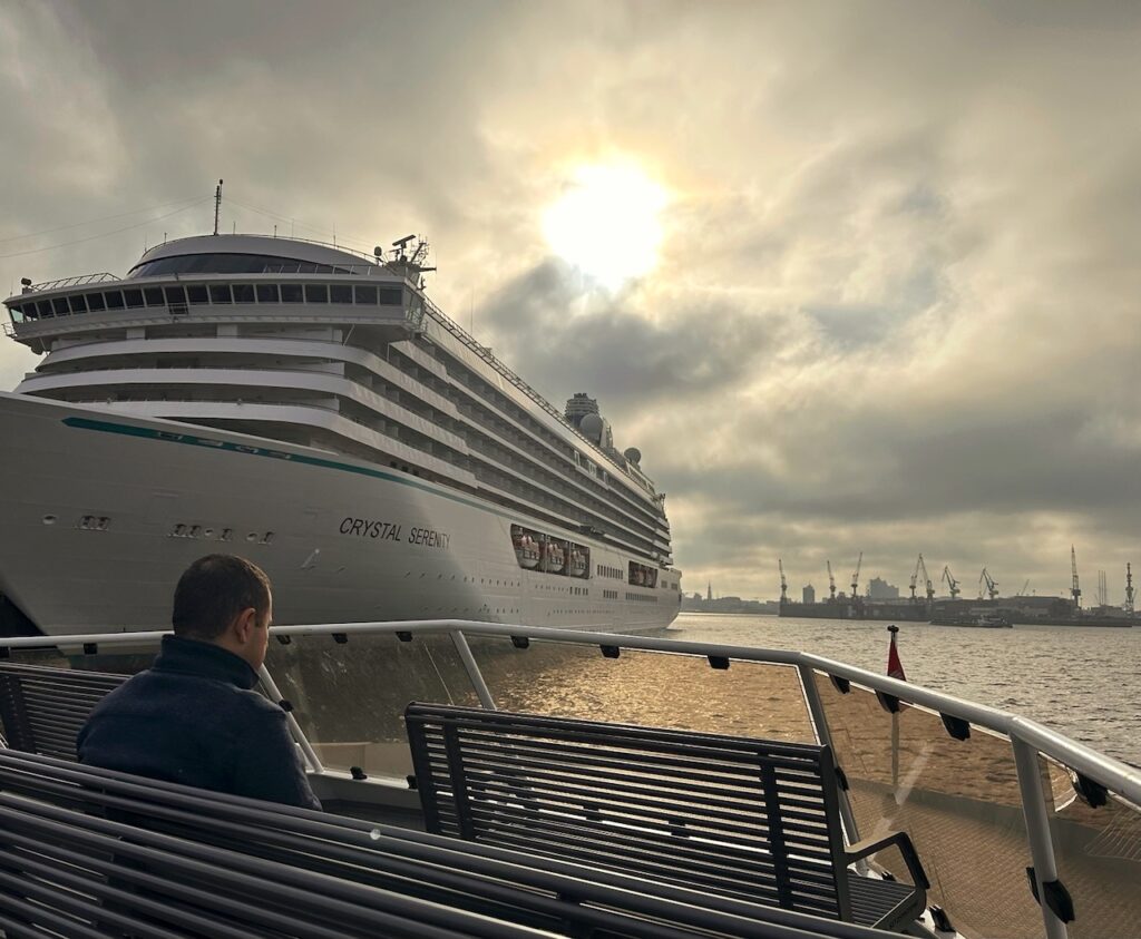 Passagier sitzt auf der Hadag Hafenfähre Linie 62 und sieht beim Sonnenaufgang links ein grosses Kreuzfahrtschiff, das Backbord kreuzt
