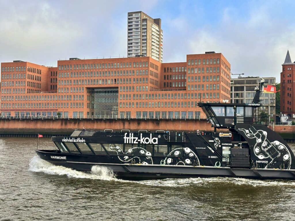 Hadag Hafenfähre Linie 62 in schwarzer Farbe und Fritz-Kola-Werbung auf der Elbe vor Altona